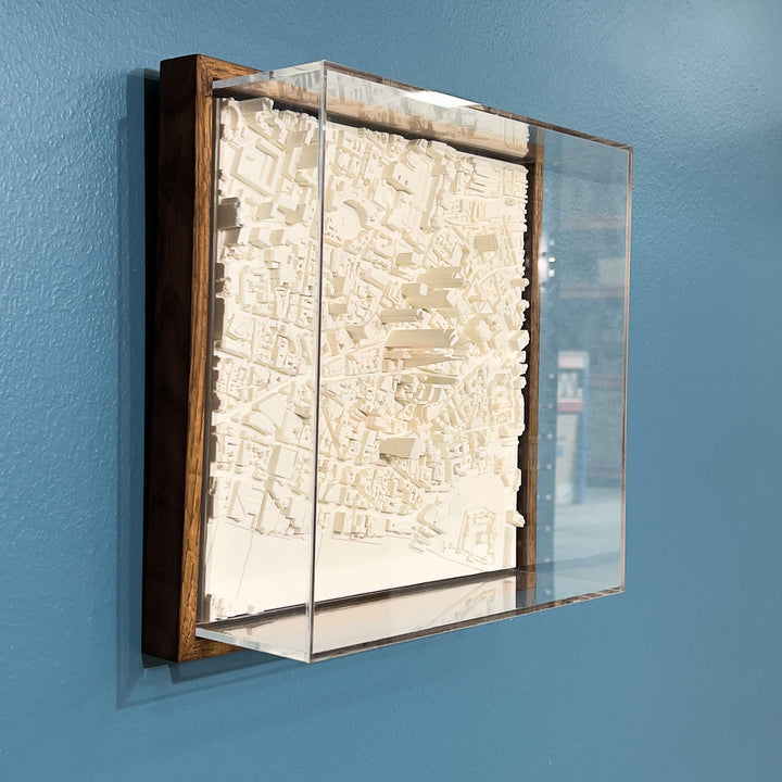 3D model of London in a dark colour oak frame with an acrylic case. London cityscape model hanging on a blue wall.