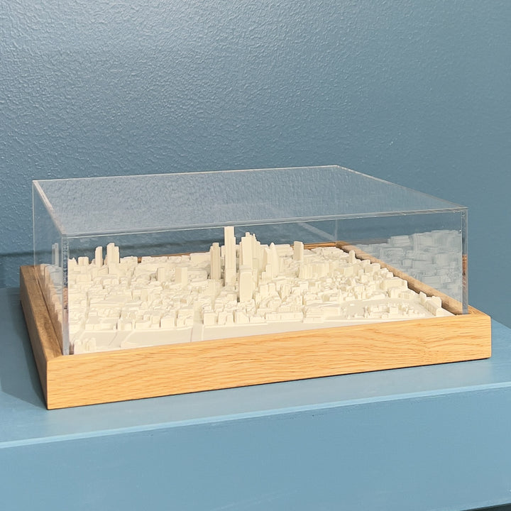 3D model of London in a light colour oak frame with an acrylic case. London cityscape model sitting on blue plinth.