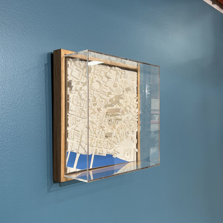 3D model of London in a light colour oak frame with river coloured blue and an acrylic case. London cityscape model hanging on a blue wall. 