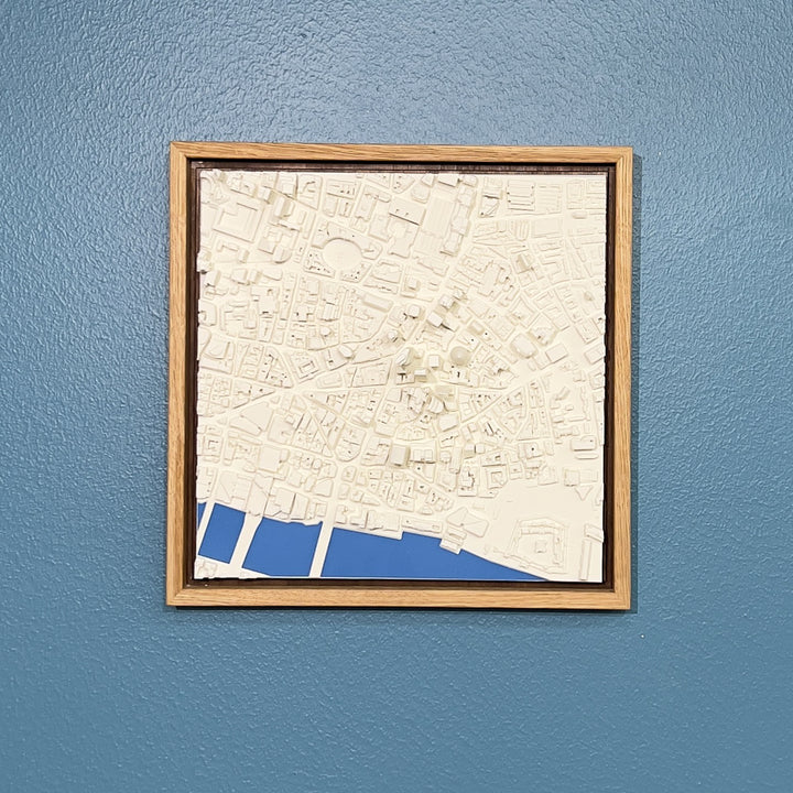 3D model of London in a light colour oak frame with river coloured blue. London cityscape model hanging on a blue wall.