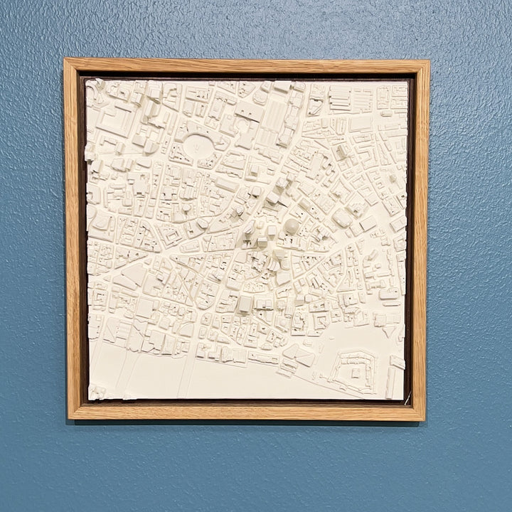 3D model of London in a light colour oak frame. London cityscape model hanging on a blue wall.